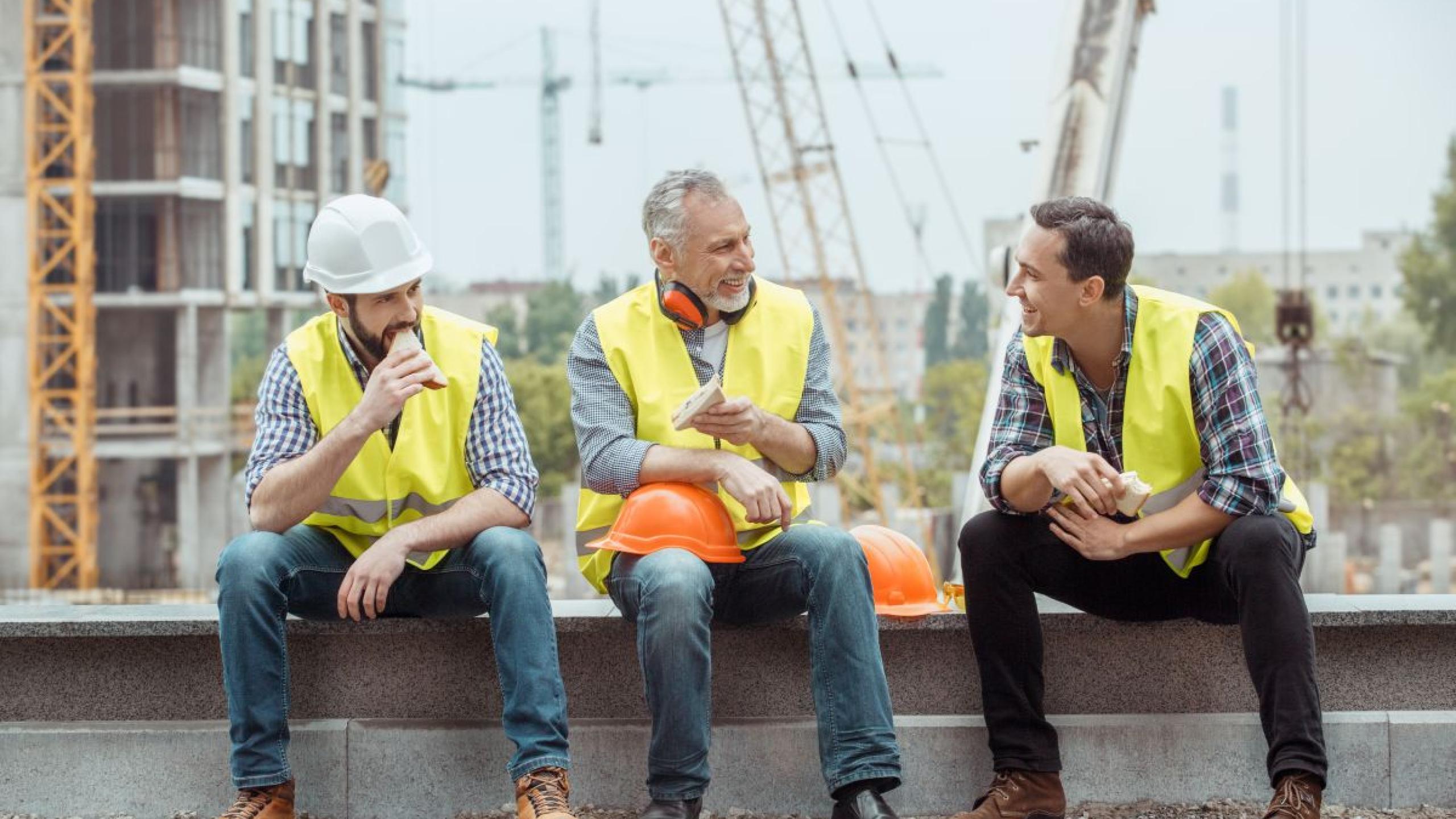 Drie arbeiders eten boterhammen op bouwplaats.